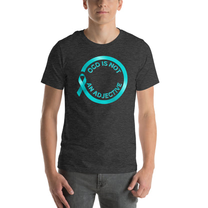 Modeling the 'OCD Is Not An Adjective' tee by NeuroNiche Design, a person stands against a plain white background wearing the shirt featuring a teal awareness ribbon on soft, dark combed cotton.