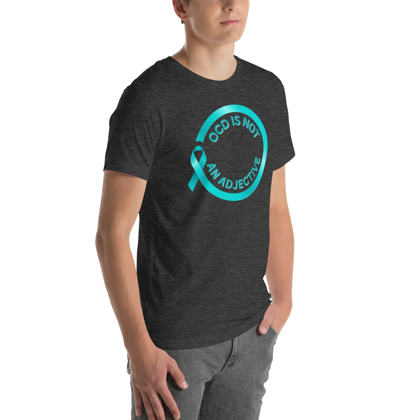 A person stands with one hand in their pocket, wearing NeuroNiche Design's "OCD Is Not An Adjective" dark gray T-shirt made from soft combed cotton, featuring a teal awareness ribbon and the slogan inside a teal circle on the front.